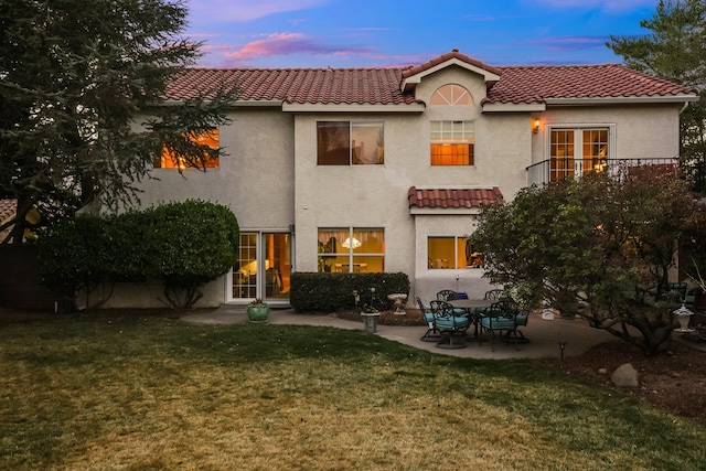 rear view of house featuring a tile roof, a lawn, a patio, and stucco siding