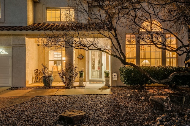 property entrance featuring a garage, a tile roof, and stucco siding