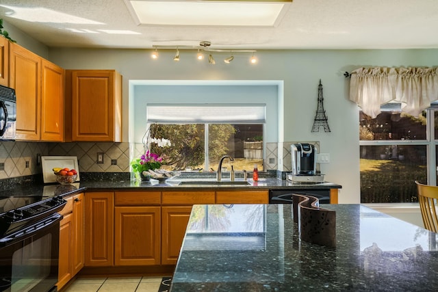 kitchen with backsplash, light tile patterned flooring, a sink, dark stone counters, and black appliances