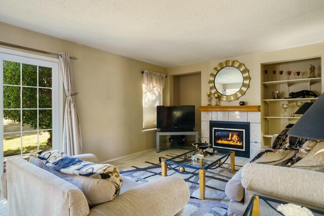 living room featuring built in shelves, baseboards, a textured ceiling, and a tiled fireplace