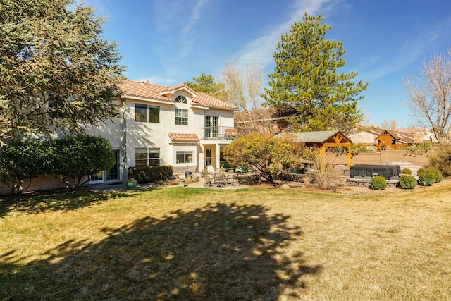 rear view of property with a patio, stucco siding, a lawn, a balcony, and a tiled roof