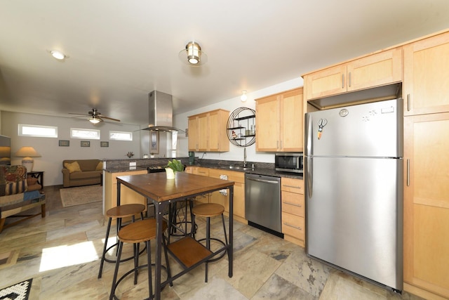 kitchen with island range hood, dark countertops, appliances with stainless steel finishes, light brown cabinetry, and a sink