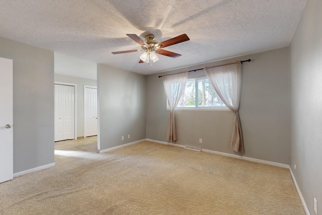 unfurnished room featuring visible vents, baseboards, ceiling fan, light colored carpet, and a textured ceiling