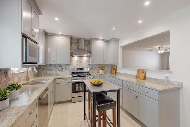 kitchen featuring backsplash, wall chimney range hood, gray cabinets, stainless steel appliances, and a sink