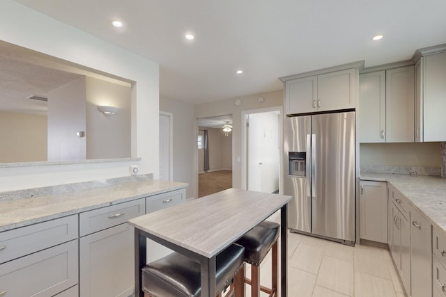 kitchen with light stone counters, recessed lighting, stainless steel refrigerator with ice dispenser, and gray cabinetry