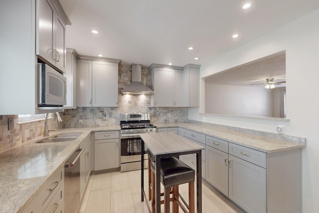 kitchen with tasteful backsplash, wall chimney range hood, gray cabinets, appliances with stainless steel finishes, and a sink