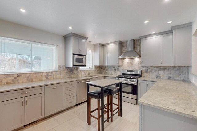 kitchen with gray cabinetry, a sink, appliances with stainless steel finishes, wall chimney exhaust hood, and backsplash