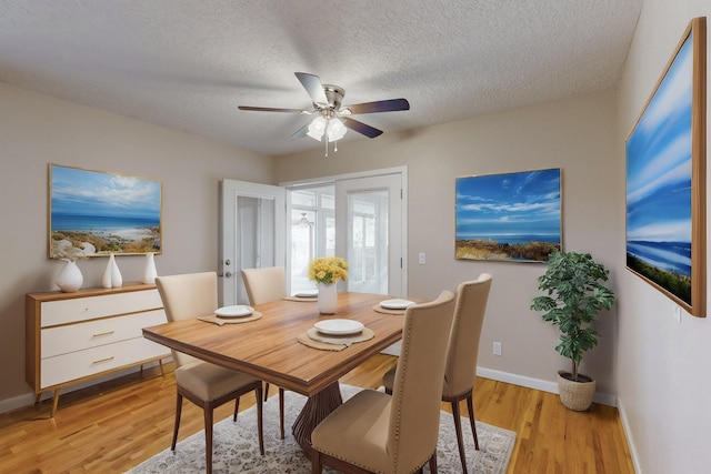 dining area featuring baseboards, ceiling fan, a textured ceiling, and light wood-style floors