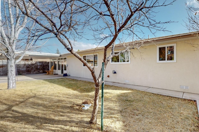 back of property featuring stucco siding, a lawn, crawl space, an attached carport, and a patio area