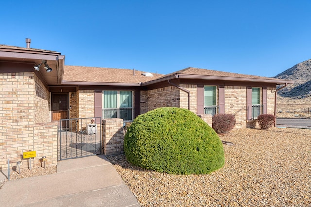 view of front of property with a mountain view, brick siding, roof with shingles, and a gate