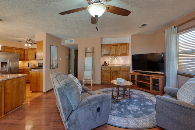 living area with visible vents, light wood-style floors, ceiling fan, and a textured ceiling