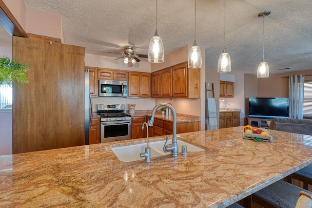 kitchen with a sink, light stone countertops, appliances with stainless steel finishes, and brown cabinetry