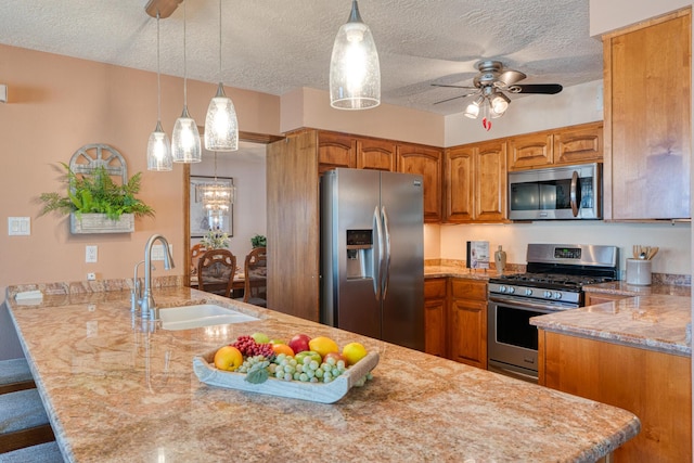 kitchen featuring brown cabinets, a ceiling fan, a sink, appliances with stainless steel finishes, and a peninsula