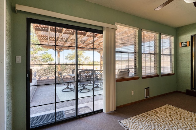 doorway with a textured wall, baseboards, carpet floors, and ceiling fan