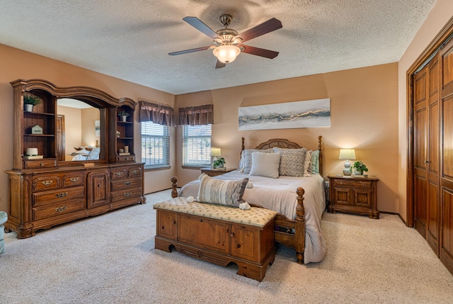 bedroom featuring a closet, light colored carpet, a textured ceiling, and a ceiling fan