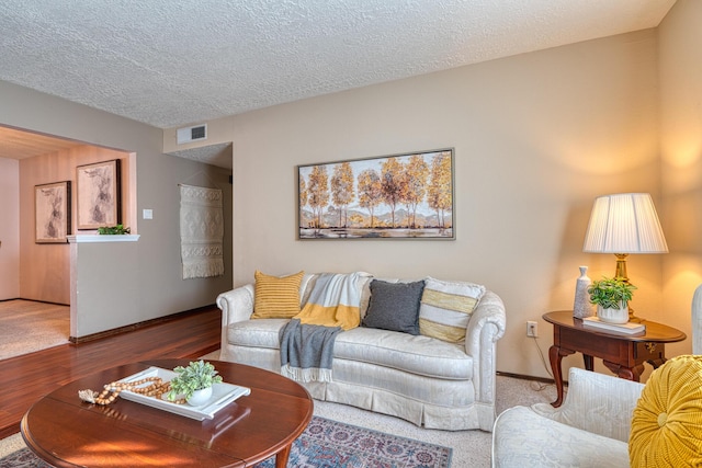 living area with visible vents, baseboards, a textured ceiling, and wood finished floors