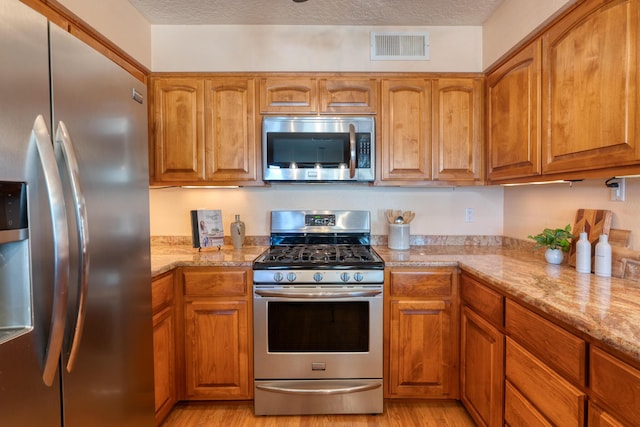 kitchen featuring stainless steel appliances, light stone countertops, visible vents, and brown cabinets