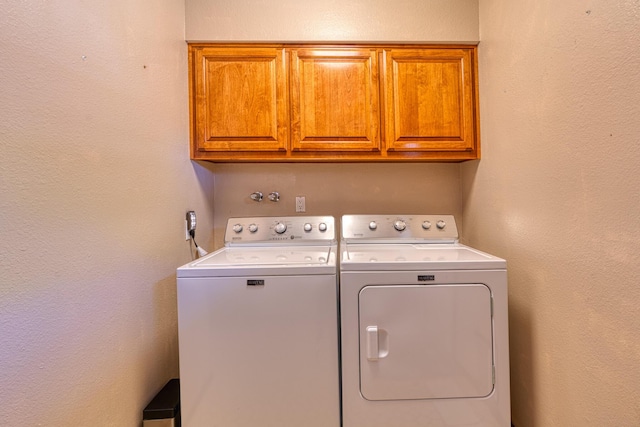 laundry room featuring cabinet space, a textured wall, and washing machine and clothes dryer