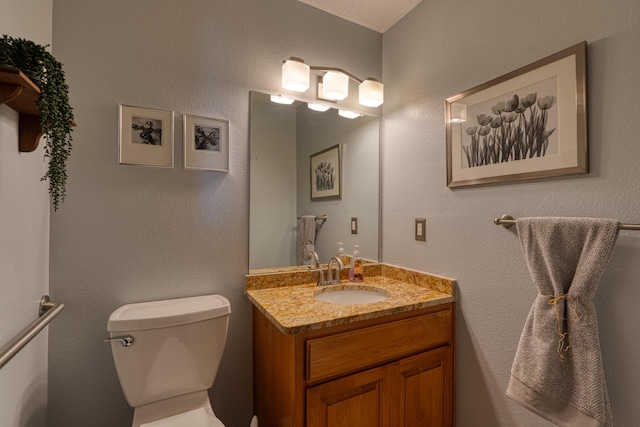 half bath featuring toilet, vanity, and a textured wall