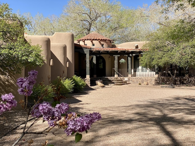 pueblo-style house with stucco siding, a tiled roof, and covered porch