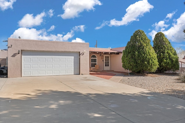 adobe home featuring a tiled roof, an attached garage, driveway, and stucco siding