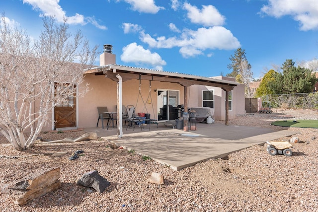 rear view of property featuring a patio, a gate, fence, stucco siding, and a chimney