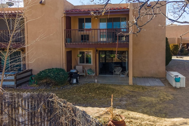 rear view of house with a balcony, a patio, and stucco siding