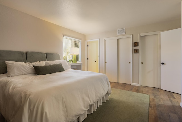 bedroom with visible vents, multiple closets, and wood finished floors