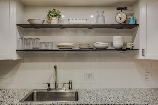 details featuring open shelves, light stone counters, decorative backsplash, white cabinets, and a sink