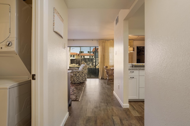 corridor with visible vents, stacked washer / dryer, baseboards, dark wood-style flooring, and a textured wall