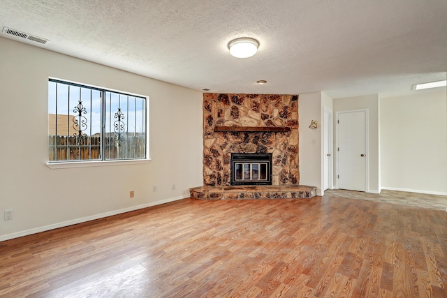 unfurnished living room with visible vents, a textured ceiling, wood finished floors, and a fireplace