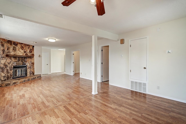 unfurnished living room featuring visible vents, baseboards, a stone fireplace, wood finished floors, and a ceiling fan