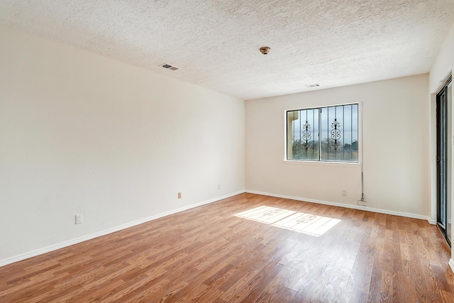 empty room featuring light wood-type flooring, visible vents, baseboards, and a textured ceiling