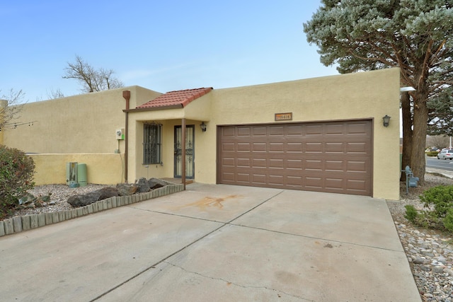 pueblo revival-style home with stucco siding, a garage, and concrete driveway