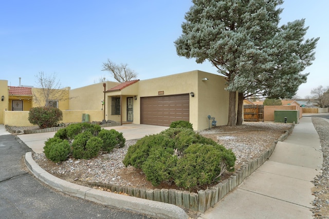 pueblo revival-style home with stucco siding, driveway, a garage, and fence