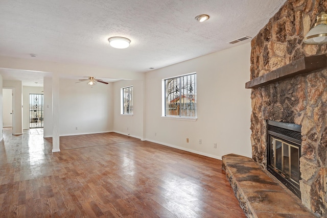 unfurnished living room with visible vents, a textured ceiling, wood finished floors, and a fireplace