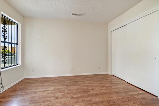 unfurnished bedroom with baseboards, visible vents, a closet, a textured ceiling, and light wood-type flooring