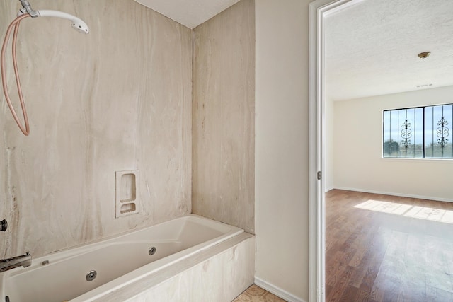 bathroom featuring a textured ceiling, a combined bath / shower with jetted tub, baseboards, and wood finished floors