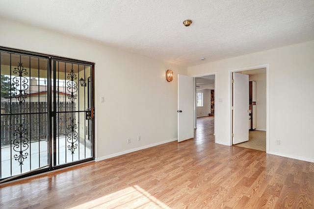 empty room featuring baseboards, a textured ceiling, a healthy amount of sunlight, and wood finished floors