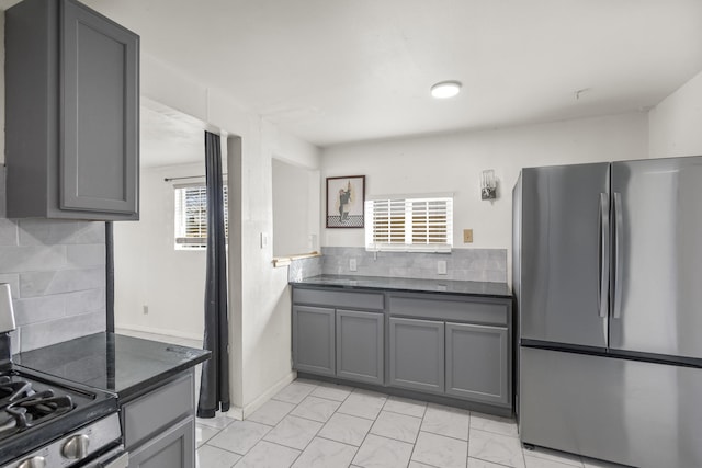 kitchen with tasteful backsplash, dark countertops, appliances with stainless steel finishes, and gray cabinetry