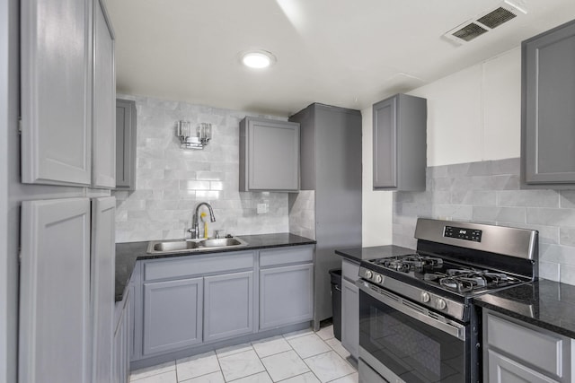 kitchen with visible vents, backsplash, stainless steel range with gas cooktop, gray cabinets, and a sink