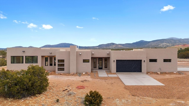 pueblo-style home with stucco siding, driveway, a mountain view, french doors, and an attached garage