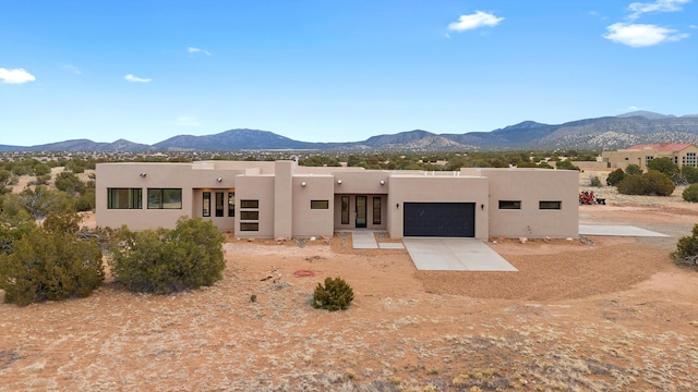 view of front of property featuring driveway, an attached garage, stucco siding, french doors, and a mountain view