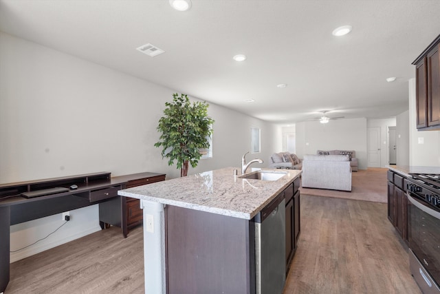 kitchen with stainless steel appliances, a sink, dark brown cabinets, light wood-style floors, and open floor plan