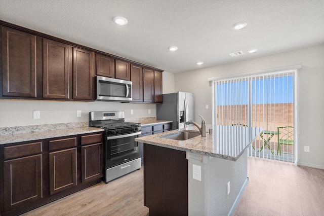 kitchen featuring visible vents, dark brown cabinets, light stone counters, stainless steel appliances, and a sink