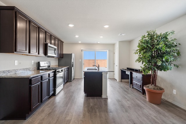 kitchen featuring dark brown cabinetry, an island with sink, light wood-style floors, and appliances with stainless steel finishes