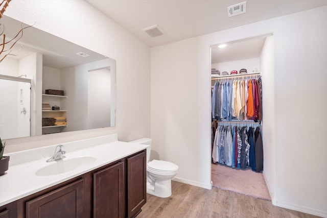 bathroom with visible vents, a walk in closet, toilet, wood finished floors, and vanity