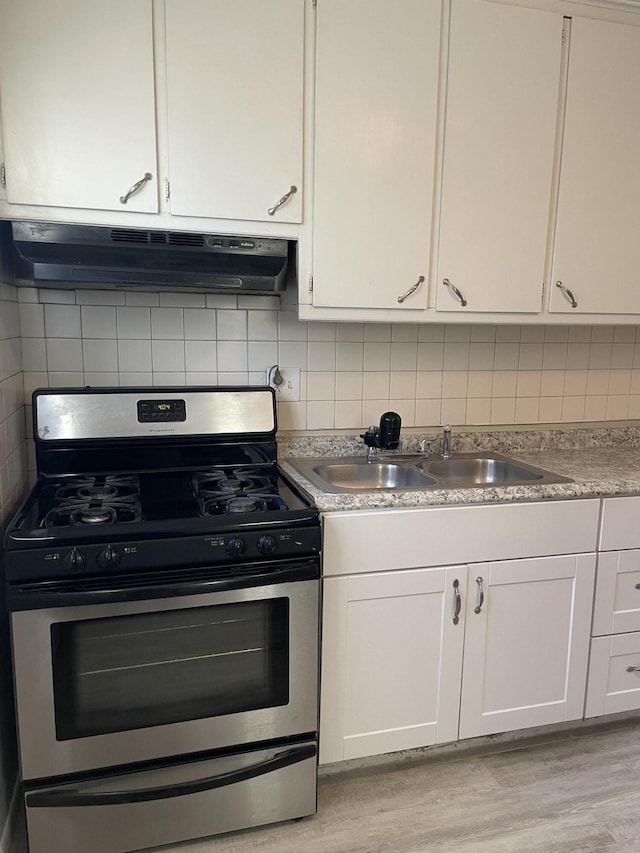 kitchen featuring stainless steel gas stove, under cabinet range hood, white cabinets, and decorative backsplash