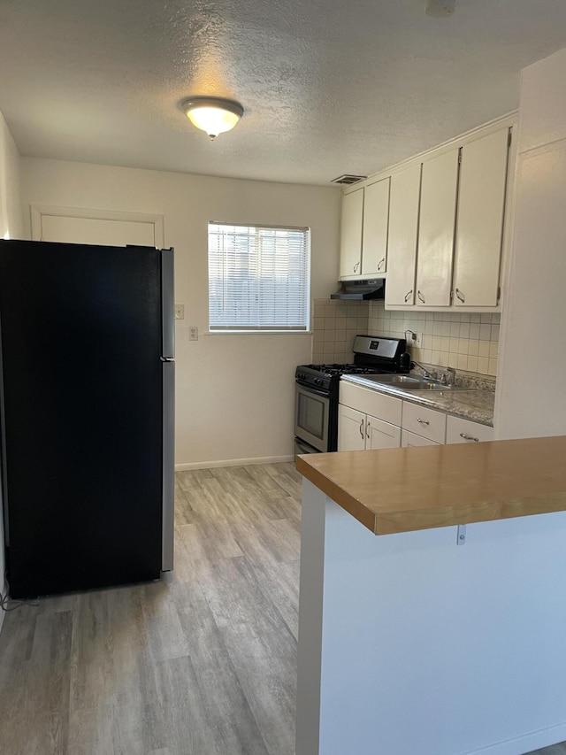 kitchen featuring light wood finished floors, tasteful backsplash, appliances with stainless steel finishes, white cabinets, and under cabinet range hood