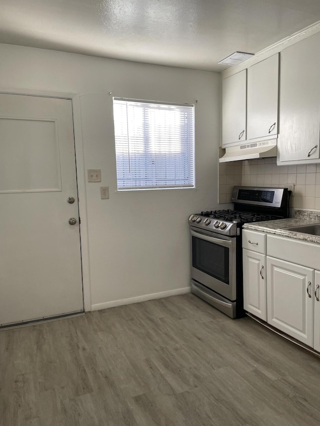 kitchen featuring under cabinet range hood, light wood-style floors, white cabinets, stainless steel gas stove, and tasteful backsplash